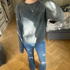 Mörkgrå stickad tröja i ullmix - Mysig mörkgrå stickad tröja med rund hals och långa ärmar. Tröjan är tillverkad i en mjuk ullmix med inslag av nylon, akryl och elastan, vilket gör den både skön och följsam. Perfekt för dig som gillar en enkel och chill stil.