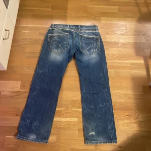 Blå jeans från Red Bridge med broderi - Säljer ett par blå jeans från Red Bridge med coola kontrastsömmar och broderade detaljer på bakfickan. Jeansen har normal passform, raka ben och slitningar för en schysst streetstil. Materialet är klassisk jeansbomull och midjan är midwaist.