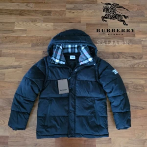 Burberry Puffer - Svart dunjacka från Burberry med klassisk Säljer en elegant och mångsidig Burberry-jacka i svart, i nyskick. Dunfodrad för värme och komfort med det klassiska rutmönstret i huvan som ger en exklusiv touch. Praktiska dragkedjefickor, avtagbar huva och diskret logopatch på ärmen.. Jackan är i princip som ny och utan defekter. En lyxig kombination av stil och funktion – perfekt för både vardag och tillfällen då du vill klä upp dig.  📦Snabb leverans - skickas samma dag📦 