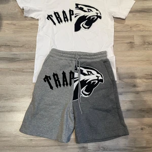 Trapstar vit t-shirt med pantertryck - Vit t-shirt från Trapstar med stor svart pantergrafik och texten 'TRAP' i fet stil över bröstet. T-shirten har rund hals och korta ärmar, tillverkad i mjuk bomull. Perfekt för dig som gillar streetwear och vill sticka ut med en unik design.