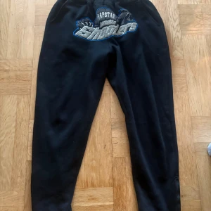 Trapstar marinblå mjukisbyxor M - Mörkblå mjukisbyxor från Trapstar med broderad text och motiv på framsidan. Byxorna har snörning i midjan och en loose passform. Materialet är mjukt och bekvämt, perfekt för chill dagar. Snygg detalj med 'London Shooters' brodyr i grått och blått.