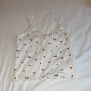 Vit ribbad linnetopp med körsbär - Supersöt vit linnetopp från H&M med tunna axelband och ribbad struktur. Toppen har ett gulligt körsbärsmönster i rött och grönt över hela tyget och en lätt vågig kant. Kommer aldrig till användning. Pris kan diskuteras 💞