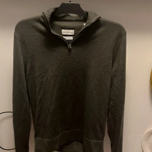 Mörkgrå merinotröja These Glory Days - Snygg mörkgrå långärmad tröja från These Glory Days i mjuk merinoull. Tröjan har half zip-dragkedja vid kragen och är perfekt för lager-på-lager. Enkel och stilren design som funkar till det mesta.