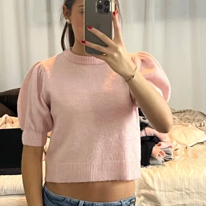 Ljusrosa stickad tröja med puffärm - Supersöt ljusrosa stickad tröja med korta puffärmar och ribbade muddar. Tröjan är croppad och har en rund halsringning. Perfekt för dig som gillar en feminin och trendig stil.