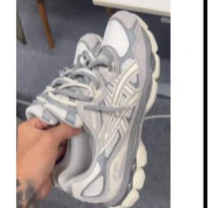 Grå och vita Asics sneakers - Säljer ett par snygga Asics sneakers i grått och vitt med klassisk logga på sidan. Skorna har snörning och en chunky sula som ger en sportig vibe. Perfekta för dig som gillar streetstyle och bekväma skor till vardags.