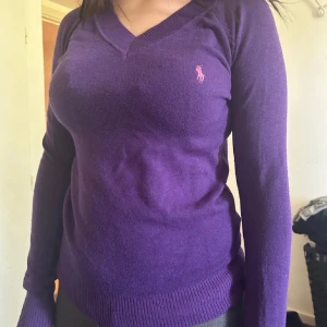 Lila v-ringad tröja från Ralph Lauren 100% Cashmere - Snygg lila v-ringad tröja från Polo Ralph Lauren 100% Cashmere med klassisk rosa logga broderad på bröstet. Tröjan är långärmad och har ribbade muddar vid ärmslut och nederkant. Perfekt för dig som gillar stilrena och tidlösa plagg. Endast swish så skickar spårbart 59❤️