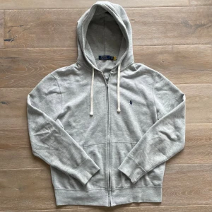 Ralph lauren hoodie - Säljer denna riktigt snygga gråa hoodie från Ralph lauren! Den är i mycket bra skick enda defekten är en liten fläck på armen (skriv för bild) storlek L och modell 180 så passar bra på allt från 175- 190 cm, den är 65 cm lång och 58 cm bred under armhålorna, hör gärna av dig vid frågor!