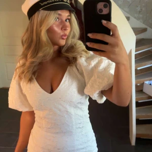 Vit kort klänning från Gina Tricot - Supersnygg vit kort klänning från Gina Tricot med puffärmar och v-ringning. Klänningen har ett strukturerat tyg med lätt glans och dragkedja bak. Perfekt för student eller sommarens alla tillfällen!