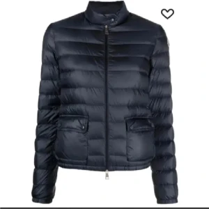 Mörkblå Moncler dunjacka med dragkedja - Snygg mörkblå dunjacka från Moncler med quiltad design, hög krage och två fickor framtill med lock. Jackan har en rak passform, lång ärm och stängs med dragkedja. Klassisk Moncler-logga på ärmen och innerfoder med märkets etikett.