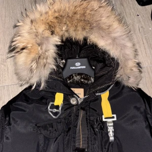 Parajumper jacka - Säljer en svart Parajumpers parkas med stor fluffig päls på huvan och coola gula detaljer. Jackan har dragkedja, knappar och flera fickor. Perfekt för kalla dagar och har en riktigt snygg streetstil.
