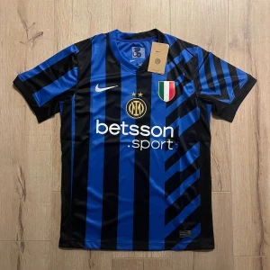 Inter Milan blå-svart matchtröja Nike S - Inter Milan fotbollströja i blått och svart med randigt mönster, tillverkad i lätt polyester. Tröjan har korta ärmar, V-ringad krage och detaljer som klubbmärke, Nike-logga, sponsortryck och italienska mästarmärket på bröstet. Snygga guldinslag och coola grafiska linjer på ryggen.