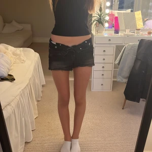 Svarta jeansshorts från Zara - Säljer ett par svarta jeansshorts från Zara med råa kanter och slitna detaljer. Shortsen har låg midja och klassisk femficksdesign. Perfekta för sommaren och lätta att matcha med allt. Snygg, avslappnad vibe!