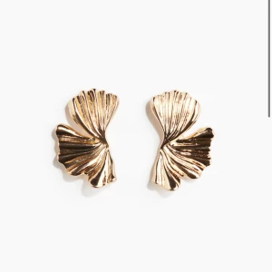 Stora guldiga statementörhängen - Säljer ett par stora, vågformade örhängen i blankt guldigt metallmaterial. De har en unik, skulptural design som påminner om veckade blad eller snäckor och sitter snyggt på örat. Perfekta för dig som vill sticka ut med accessoarerna. Använda upp till 1 - 2 gånger , originalpris, 99 sek.