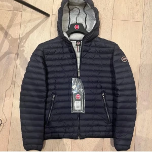 Mörkblå  dunjacka från Colmar med huva - Snygg mörkblådunjacka från Colmar med huva. Jackan har quiltad design och Colmar-logga på ärmen. Perfekt för kyliga dagar och har en stilren look som passar till det mesta.