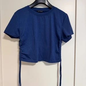 Marinblå croppad topp från SHEIN - Säljer en marinblå croppad topp från SHEIN med korta ärmar och snörning på sidorna. Enkel och stilren design i mjuk bomull, perfekt för att skapa en chill och trendig look. Passar dig som gillar att styla med jeans eller kjol.