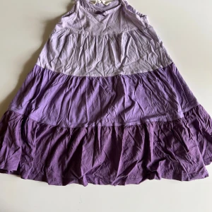 Lila klänning från H&M - Supersöt lila klänning från H&M med flera lager i olika nyanser av lila. Klänningen har smala axelband och en liten rosett framtill. Tillverkad i mjuk bomull, perfekt för varma dagar.