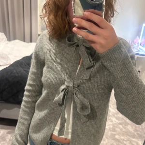 Grå ribbad kofta med knyt - Mysig grå ribbad kofta med långa ärmar och två snygga knytband framtill. Endast använd 2-3 gånger!