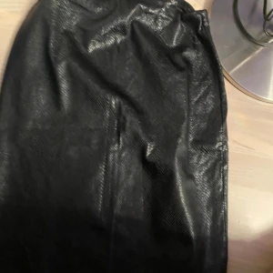 Svart skinnimitation kjol Boohoo - Säljer en svart kort kjol från Boohoo i skinnimitation med lätt glansig yta och rak passform. Kjolen har dragkedja i sidan och en stilren look som passar till många olika outfits.