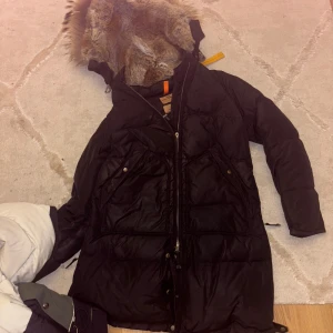 Svart Parajumpers dunjacka med päls - Säljer en svart Parajumpers dunjacka med pälsfodrad huva och ikonisk gul rem vid kragen. Jackan har flera fickor, dragkedja och snygga detaljer som PJS-märke på ärmen. Perfekt för kalla vinterdagar och riktigt varm.