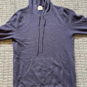 John Henric Kashmir hoodie - Mysig marinblå hoodie i 100% kashmir från John Henric. Tröjan har huva med snörning, magficka och långa ärmar. Perfekt för dig som vill ha en lyxig och stilren look med extra komfort. Nypris 2500kr