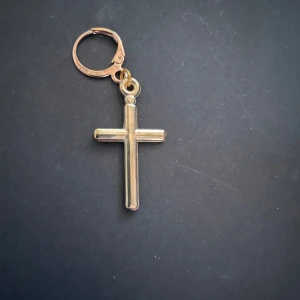 By prisförslag- 1 st Guldigt kors örhänge - Snyggt örhänge med kors i guldtonad nyans. Korset har en enkel och stilren design med rundade kanter och hängs i en klassisk öronkrok. Perfekt för dig som gillar statement-smycken med religiös touch.