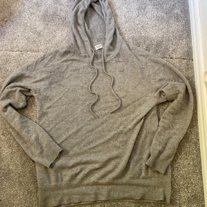 Kashmir Hoodie - Mjuk och lyxig grå hoodie från Rose & Born i 100% cashmere. Tröjan har huva med snörning, ribbade muddar och lång ärm. Perfekt för dig som vill ha en chill och stilren look med premiumkänsla. Snyggt basic-plagg som funkar året runt.