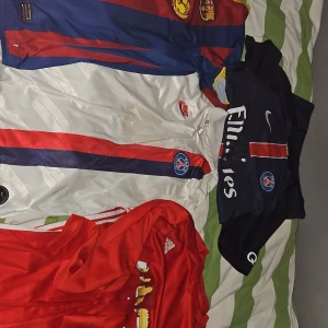 Tre fotbollströjor: PSG, Barcelona, United - Säljer tre snygga fotbollströjor: en blå och röd Barcelona-tröja med klubbmärke, en vit PSG-tröja med röd och blå rand samt Nike-logga, och en mörkblå PSG-tröja med röd rand och Emirates-tryck. Dessutom en röd Manchester United-tröja från Adidas. Perfekt för dig som älskar fotboll!
