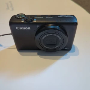Canon PowerShot S90 - Canon PowerShot S90 kompaktkamera med 3.8x zoom, bildstabilisering och tydlig LCD-skärm. Kameran är i gott skick, inga repor eller skador. Perfekt för både vardagsfotografering och resor. Alla knappar och funktioner  fungera som de ska. Original laddare och batteri ingår 