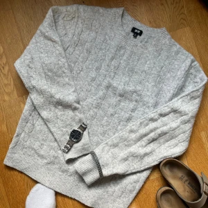 Ljusgrå kabelstickad tröja Uniqlo XS - Mysig ljusgrå kabelstickad tröja från Uniqlo i storlek XS. Tröjan har rund halsringning, ribbade muddar och är tillverkad i en mjuk ullblandning. Perfekt för lager-på-lager och chill höst- och vinterstil.