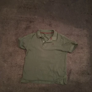 Olivgrön Scalpers pikétröja - Olivgrön pikétröja från Scalpers med klassisk krage och två knappar framtill. 