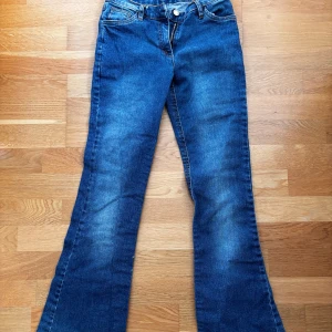Blå bootcut jeans med dragkedja - Säljer ett par klassiska blå bootcut jeans med snyggt slitna detaljer och dragkedja framtill. Jeansen har normal passform och är tillverkade i tåligt denimtyg. Låg midja. Finns inget hål för gylfknappen så det måste man göra själv! Passar xxs-xs 