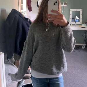 Grå stickad tröja med loose fit - Mysig grå stickad tröja med avslappnad, loose passform och rund halsringning. Perfekt att slänga på sig över en t-shirt för en chill look. Långärmad och enkel design som funkar till jeans eller leggings.