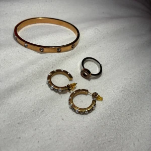 Edblad smycken  - Säljer ett snyggt guldarmband med infällda stenar, ett par guldfärgade creoler med små pärlor och en svart ring med gulddetalj. Perfekt för dig som gillar att mixa olika smycken och vill ha en lyxig touch på din stil. Allt från Edblad, pris kan diskuteras vid snabb affär.