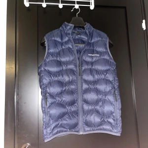 Blå dunväst Peak Performance 170 - blå dunväst från Peak Performance med quiltad design och dragkedja framtill