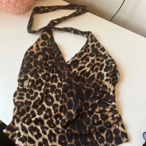 Leopardmönstrad halterneck topp Romwe - Säljer en snygg leopardmönstrad halterneck topp från Romwe i storlek XS. Toppen har omlott-skärning framtill och knytband i nacken. Materialet är mjukt och stretchigt, perfekt för att sticka ut med ett djurmönster. Färgerna går i brunt, beige och svart.