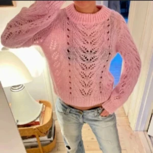 Ljusrosa stickad tröja - Superfin ljusrosa stickad tröja med snyggt hålmönster och bred ribbad krage. Tröjan har långärmade ärmar och en lite loose passform, perfekt att styla med jeans. Mjuk och fluffig känsla, riktigt mysig för kyligare dagar.