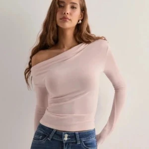 Ljusrosa offshoulder topp - Säljer en ljusrosa, croppad tröja med asymmetrisk off shoulder design och långa ärmar. Toppen har en tight passform och är tillverkad i ett mjukt, stretchigt material som sitter snyggt mot kroppen. 