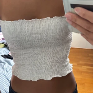 Vit bandeau tubtopp från Bik Bok XS - Säljer en vit bandeau tubtopp från Bik Bok i storlek XS. Toppen är smockad med elastisk struktur och har vågiga kanter upptill och nedtill. 