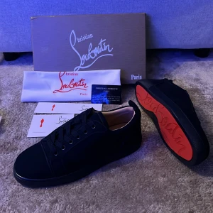 Mörkblåa sneakers från Christian Louboutin - Snygga mörkblåa sneakers från Christian Louboutin med ikonisk röd sula. Skorna har rund tå, snörning och är tillverkade i ett lyxigt material med diskreta detaljer. Perfekta för dig som vill sticka ut med en exklusiv touch.