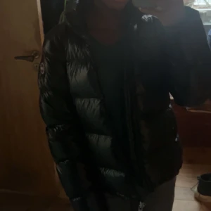 Svart pufferjacka med huva - INTRESSEKOLL!!                                                 Säljer en svart pufferjacka från Colmar med glansig finish och huva. Jackan har en klassisk quiltad design och en logga på ärmen. Perfekt för kalla dagar när du vill hålla värmen och ändå se snygg ut.