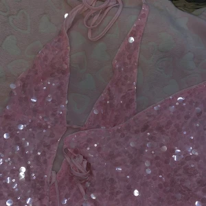 Rosa paljett set med halterneck - Rosa set med kjol och topp med glittriga paljetter och halterneck-knytning. har en djup urringning och tunna band som knyts i nacken. Perfekt för dig som vill sticka ut med extra glitter och feminin stil. Passar S/m för man knyter den i sin egen storlek typ