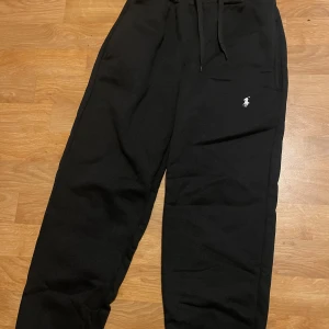 Svarta mjukisbyxor från Polo Ralph Lauren - Svarta mjukisbyxor från Polo Ralph Lauren med klassisk broderad logga i vitt på benet. Byxorna har dragsko i midjan och är tillverkade i mjukt bomullsmaterial. Perfekta för en chill och avslappnad stil.