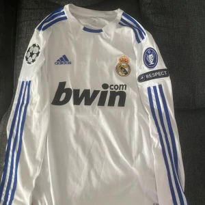 Real Madrid långärmad retro fotbollströja Ronaldo  - Säljer en ikonisk långärmad Real Madrid fotbollströja med Ronaldo 7 på ryggen. Tröjan är vit med blå ränder på ärmarna, Champions League-patchar och klubbmärke på bröstet. Materialet är lätt och andas, perfekt för match eller samling. Den har använts ett fåtal gånger 