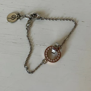 Silverfärgat armband från Edblad - Snyggt armband från Edblad i silverfärgad metall med en tunn kedja och en rund cirkelberlock i rosegild dekorerad med gnistrande stenar. Sparsamt använt. 