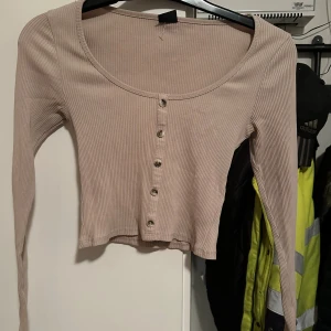 Beige ribbad topp från Gina Tricot strl: S - Säljer en beige ribbad topp från Gina Tricot i storlek S. Toppen har lång ärm, croppad passform och knappar framtill. Den är tillverkad i ett stretchigt material och har en rundad urringning. Perfekt att styla med jeans eller kjol.