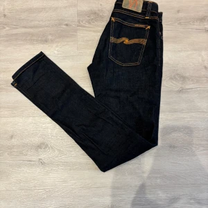 Mörkblå Nudie Jeans 28/32  - Snygga mörkblå jeans från Nudie Jeans i modellen skinny. Klassisk femficksdesign med orange kontrastsömmar och Nudie-logga på bakfickan. Jeansen är tillverkade i slitstarkt denim och har en smal passform som sitter tajt längs benen.
