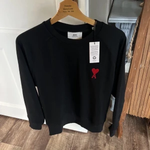 Svart tröja från Ami - AMI Paris Sweatshirt – Helt ny! Säljer denna stilrena svarta sweatshirt från AMI Paris, inköpt för 2000 kr. Tröjan är helt ny, aldrig använd och har fortfarande tags kvar. 	•	Modell: Ami de Coeur Sweatshirt 	•	Färg: Svart med rött hjärta och “A”-brodyr 	•	Storlek: M 	S Material: Mjuk och högkvalitativ bomull 	•	Nypris: 2000 kr  Perfekt för dig som vill ha en klassisk och tidlös sweatshirt med en snygg detalj. Passar både vardags och casual-stil.  Pris: 1000.                   GÅR MED PÅ BYTEN 