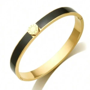 Svart och guldigt armband med romerska siffror - Snyggt armband i svart och guld med en rund detalj i mitten som har romerska siffror runt om. Armbandet har en stilren och modern design, perfekt för att ge din outfit lite extra edge. Metallmaterial och blank finish.