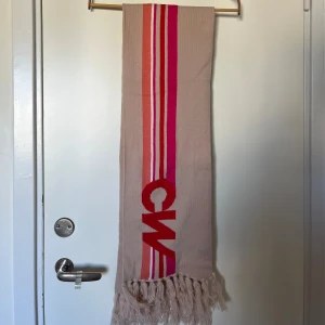 Beige halsduk Carin Wester med rosa ränder - Snygg beige halsduk från Carin Wester med långa fransar och ränder i rosa, rött och orange. Perfekt i höst och vinter. Ca 160 cm lång. Oanvänd, nyskick. 