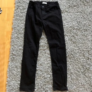 Svarta jeans från Lindex - Svarta jeans från Lindex med fem fickor och hällor för bälte. Jeansen har normal midja och är tillverkade i stretchig bomullsblandning för en bekväm passform. Perfekta för dig som gillar en stilren och enkel look.